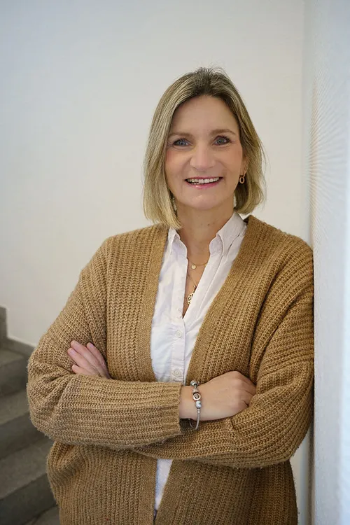 Christiane Roßner, Mitarbeiterin im Anwaltsbereich der Anwalt- und Notarkanzlei Illner in Bochum, lehnt an einer Wand und lächelt freundlich den Betrachter an.
